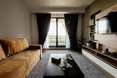 Kahverengi kanepe, sehpa ve televizyon ünitesi olan oturma odası, balkon kapısından gün ışığı