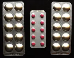 Siyah zemin üzerinde üç blister ambalajda tabletler, yakın çekim (marka okunmuyor)