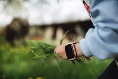 Bilekte pembe kayışlı akıllı saat, elde bir tutam ot